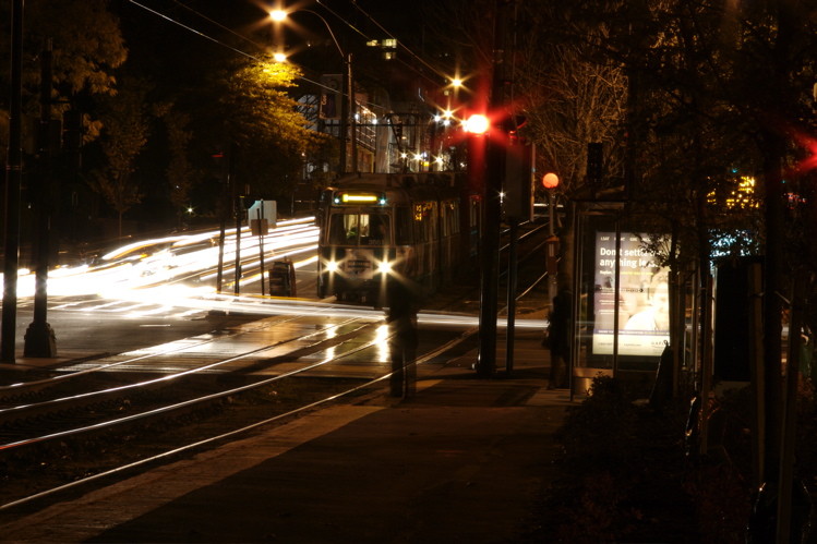 Photo of An MBTA green line train waits as vehicular traffic zips by on the C branch